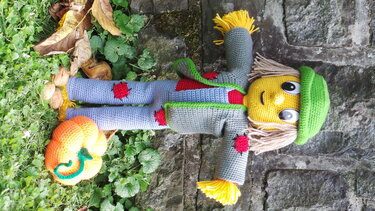 Amigurumi-Vogelscheuche mit grüner Mütze, grauem Mantel und kleinem gehäkelten Kürbis