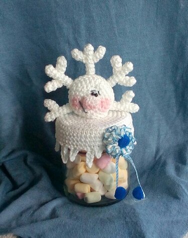 Glas mit Marshmallows und gehäkeltem weißen Schneeflocken-Deckel mit Gesicht und blauer Rosette