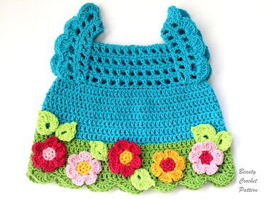 Turquoise crocheted baby dress with a green 'grass' border and colorful 3D flower and leaf appliqués.