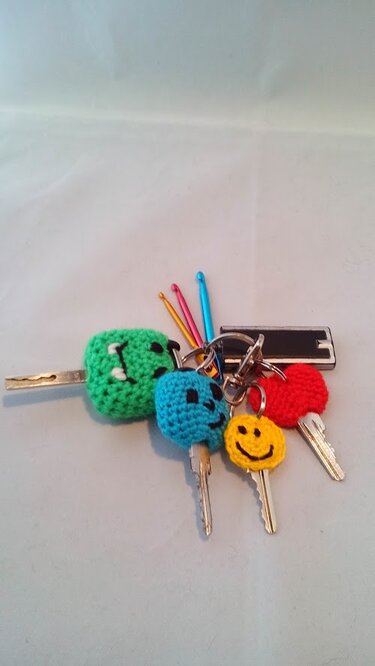 Schlüsselbund mit selbstgemachten gehäkelten Anhängern (Smiley, Herz, Monster, blauer Kreis) und bunten Häkelnadeln