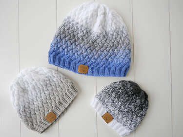 Drei gestrickte Mützen in Blau-, Grau- und Weißtönen mit Farbverlauf und Strukturmuster auf hellem Hintergrund