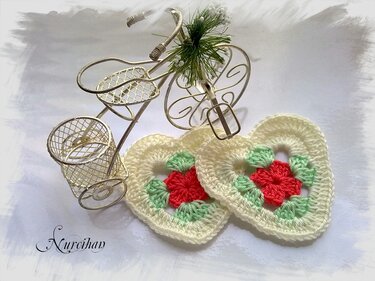 zwei zarte gehäkelte Herzen in Creme mit roter Blüte und grünen Blättern