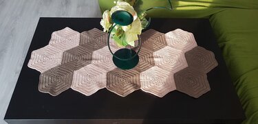 Modularer Tischläufer aus aneinandergereihten gehäkelten Hexagonen in hellen Naturtönen und Taupe auf dunkler Tischplatte mit grünem Kerzenhalter