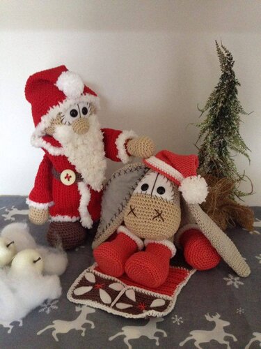 Gehäkelter Weihnachtsmann und liegender Amigurumi-Esel mit Weihnachtsmütze vor Mini-Tannenbaum