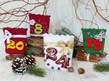 Gehäkelte Advents‑Taschen in Rot, Weiß und Grün mit Filz‑Zahlen, Perlen und Schleifen, dekorativ arrangiert mit Tannenzweigen und Zapfen