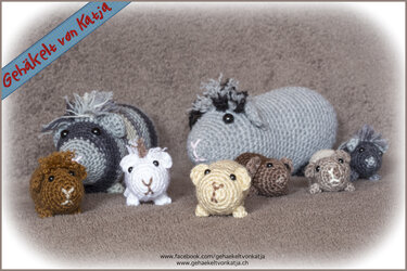 Sieben gehäkelte Meerschweinchen-Amigurumi in Grau, Braun und Beige auf einem weichen Untergrund