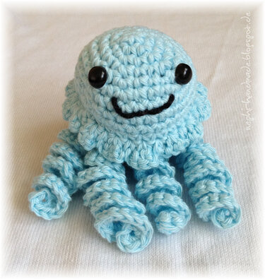 Pastellblaue gehäkelte Amigurumi-Qualle mit lächelndem Gesicht und gedrehten Tentakeln