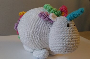 Weißes gehäkeltes Einhorn-Amigurumi mit buntem Horn und Mähne, seitliche Ansicht