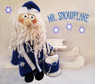 Gehäkelte Amigurumi-Figur „Mr. Snowflake“ in Blau-Weiß mit langem, lockigem Bart, Mütze und Tasche vor einem Holzschlitten.
