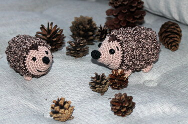 Zwei niedliche gehäkelte Igel zwischen Tannenzapfen auf Stoff