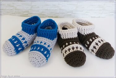 Zwei Paar gehäkelte Kinderschuhe in Blau/Grau und Braun/Beige nebeneinander auf hellem Untergrund