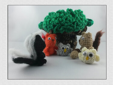 Gehäkelte Amigurumi-Waldtiere und Baum auf hellem Hintergrund: Stinktier, Eichhörnchen, orangefarbene Figur und zwei Eulen mit Wackelaugen.