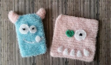 Zwei flauschige gehäkelte Monster-Quadrate in Blau und Rosa auf Holz