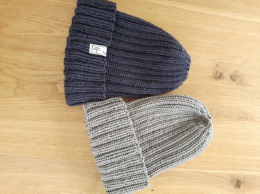 Zwei gestrickte Beanies, eine grau und eine dunkelblau, mit Umschlagbündchen auf Holzuntergrund