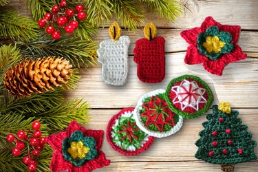 Gehäkelte Weihnachtsobjekte wie Kerzen, Sterne, Untersetzer und ein Tannenbaum auf Holz, umgeben von Tannengrün und Zapfen.