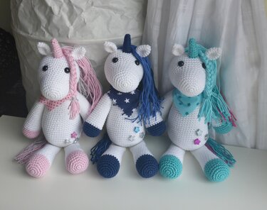 Drei gehäkelte Einhorn‑Amigurumi nebeneinander in rosa, dunkelblau und mintfarbenen Akzenten