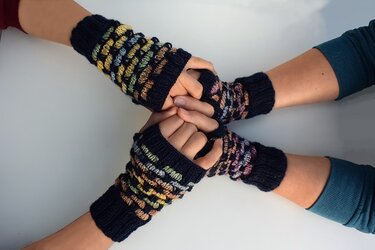 Vier Hände mit dunkelblauen, gestrickten Armstulpen mit mehrfarbigem Streifenmuster