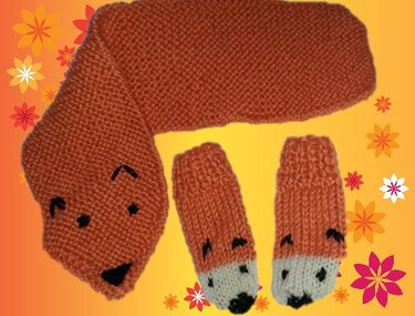 Gestricktes orangefarbenes Fuchs‑Set mit Schal in Fuchsform und zwei passenden Fäustlingen vor gelbem, floral dekoriertem Hintergrund.