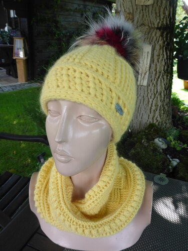 Schaufensterpuppe trägt gelbe gehäkelte Bommelmütze und passenden Loop‑Schal.