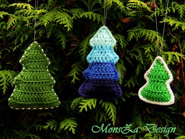 Drei gehäkelte Weihnachtsbaum-Anhänger in Grün- und Blautönen an Zweigen hängend