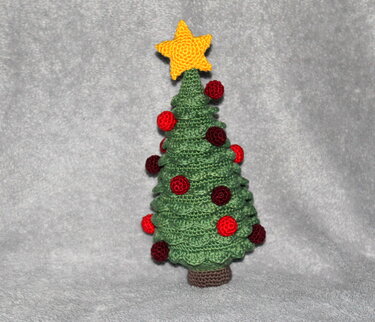Gestufter gehäkelter Weihnachtsbaum mit roten Kugeln und gelbem Stern auf grauem Stoff