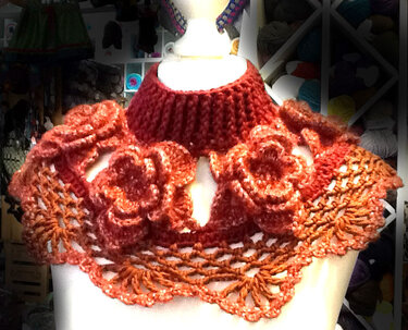 Gehäkelter Kragenschal in Orange mit geripptem Kragen und drei gehäkelten Blumen auf einer Schaufensterpuppe