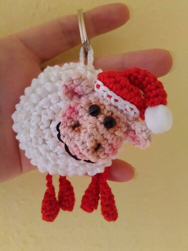 Gehäkelter weißer Schaf-Schlüsselanhänger mit roter Nikolausmütze, gehalten von einer Hand