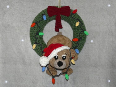 Crochet door wreath with a brown amigurumi dog wearing a Santa hat and decorative crochet lights