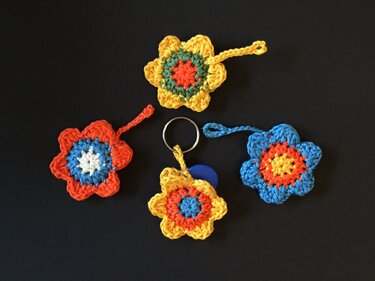 Vier bunte gehäkelte Blumen, eine mit Schlüsselring, auf schwarzem Hintergrund.