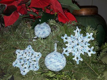 Hellblau-weiße gehäkelte Schneeflocken und Kugeln auf Tannengrün, Weihnachtsstern im Hintergrund