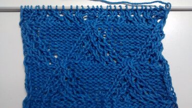 Blaue gestrickte Probe mit Rautenmuster und Lochreihen auf Nadel