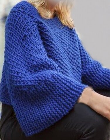 Grob gestrickter blauer Oversize-Pullover mit weiten Ärmeln an sitzender Person