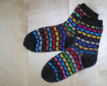 Paar Knöchelsocken mit schwarzer Ferse und Spitze und mehrfarbigem Blockmuster auf hellem Holzboden