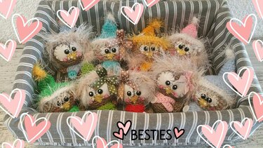 Handgefertigte, gehäkelte Eulen-Amigurumis in verschiedenen Farben, sitzend in einem graugestreiften Korb