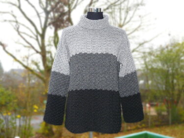 Gehäkelter Rollkragenpullover in drei Grautönen auf Schneiderpuppe.
