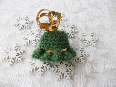 Grüne gehäkelte Weihnachtsglocke mit goldenem Band auf weißen Holzschneeflocken