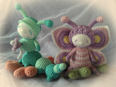 Handgehäkelte mintgrüne Raupe und lila-rosa Schmetterling (Amigurumi) auf hellem Tuch