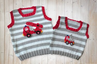 Two knitted baby and kids vests with grey and off-white stripes, red trim and red fire truck appliqués on a wooden background.