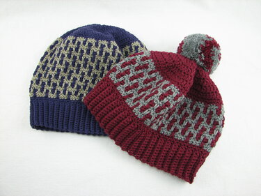 Zwei gehäkelte Mützen mit Gittermuster – dunkelblaue Beanie und bordeauxrote Bommelmütze.