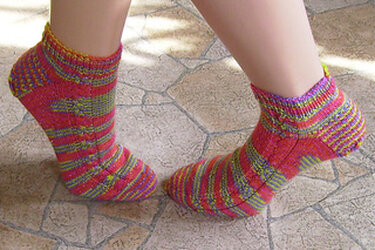 Füße in bunten gestrickten Knöchelsocken mit Ringelmuster auf gefliestem Boden