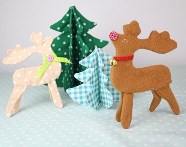 Zwei genähte Rentierfiguren aus Stoff und Filz vor kleinen genähten Stofftannen
