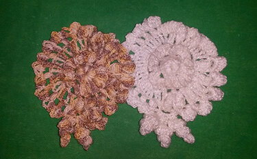 Zwei gehäkelte Blütenapplikationen, eine weiß und eine braun meliert, auf grünem Stoff