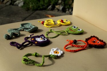 Bunte gehäkelte Lesezeichen in Form von Eule, Frosch, Smiley, Löwe, Blatt und Gänseblümchen auf hellem Untergrund