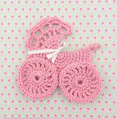 Rosa gehäkelte Kinderwagen-Applikation mit Schleife auf gemustertem Hintergrund
