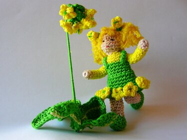 Gehäkelte Puppe in grünem Kleid mit gelben Haaren und Blume am Stiel