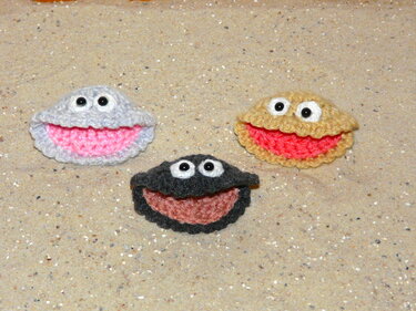 Drei gehäkelte Amigurumi-Muscheln mit Augen auf Sand