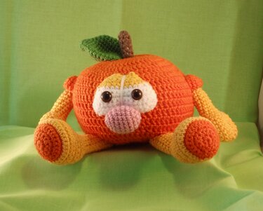 Gehäkelte Orangenfigur mit Augen, rosa Nase, Armen, Beinen, Blatt und Stiel