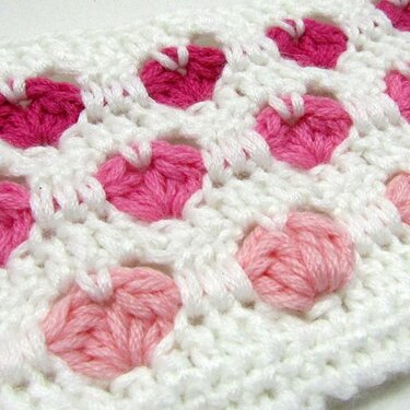 Nahaufnahme eines gehäkelten Stoffes mit rosa Herzmotiven auf weißem Grund