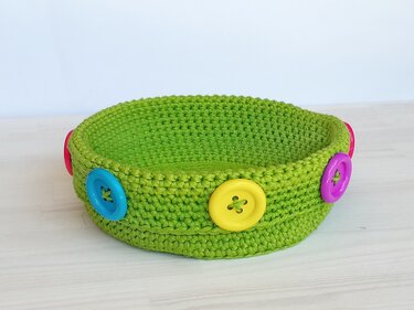 Runder gehäkelter grüner Korb mit bunten Knöpfen