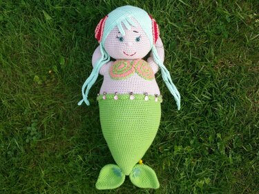 Handgehäkelte Amigurumi-Meerjungfrau mit hellgrünem Schwanz und mintgrünen Haaren auf Gras